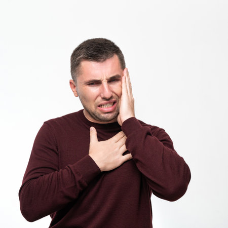 A man suffers from a toothache, portrait on a white background, painful facial expression due to toothache or dental disease.の写真素材