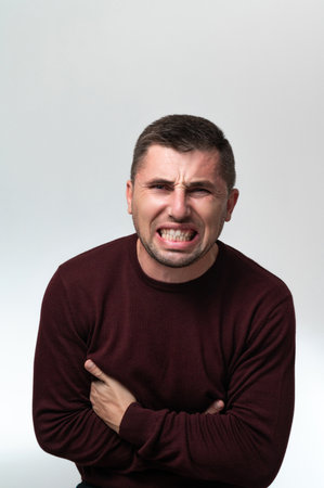 A man touches his stomach with two hands, on a white background with copy space, Stomach pain in a...