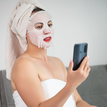 Facial skin cleansing procedure using a cosmetic mask, woman talking on the phone online, women's tricks and beauty.の写真素材