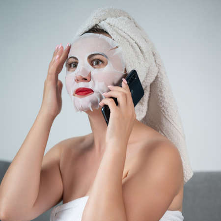A woman is talking on the phone at home, a woman with a mask on her face and a towel is sitting on...
