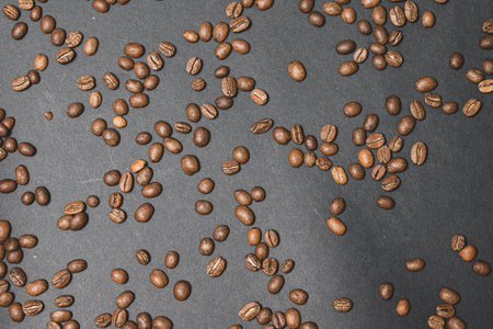 Evenly scattered coffee beans on a black background, roasted brown aromatic coffee beans.