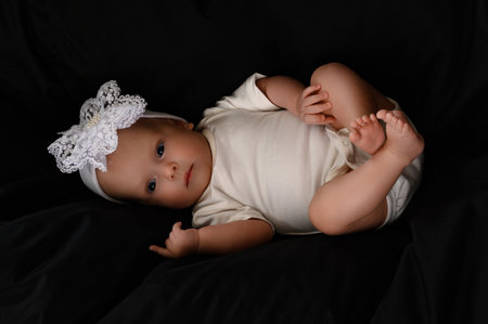 Ivano-Frankivsk, Ukraine, May 8, 2022: A newborn baby girl with a bandage on her head lies on a large black pillow, the pillow as a background.のeditorial素材
