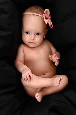 Ivano-Frankivsk, Ukraine, May 8, 2022: A newborn baby girl with a bandage on her head lies on a large black pillow, the pillow as a background.のeditorial素材