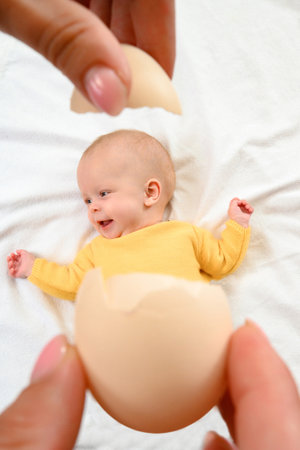 Ivano-Frankivsk, Ukraine, May 8, 2022: a newborn baby girl lying on a bed, a baby girl with an eggshell, the idea of a child with an egg.のeditorial素材