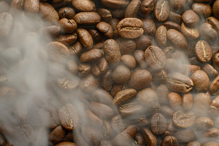 Black coffee beans with light smoke from steam, texture of coffee beans, copy space and place for...
