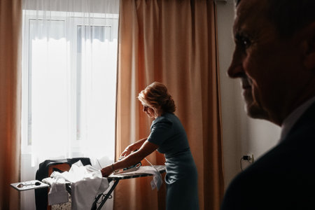 Ivano-Frankivsk, Ukraine October 2, 2022: Ukrainian traditions at a wedding, mother ironing the groom's shirt, groom's morning.のeditorial素材
