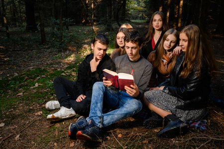 Ivano-Frankivsk, Ukraine October 14, 2022: teenage schoolchildren reading a book in the forest, a group of children in the park, a group of classmates in the autumn forest.のeditorial素材
