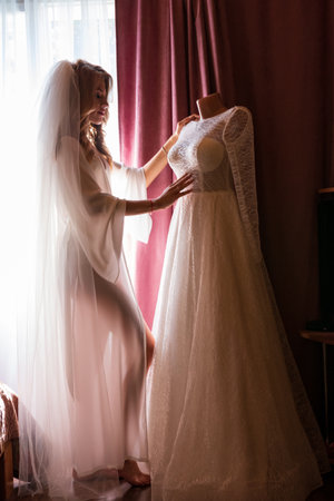 Ivano-Frankivsk, Ukraine, August 1, 2021: a bride looks at her dress by the window, A white wedding dress for the bride on her wedding day.のeditorial素材