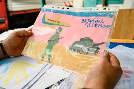 Kyiv, Ukraine July 1, 2022: Children's drawings on the theme of war, Ukrainian defender holds drawings from children in his handsのeditorial素材