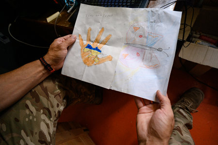 Kyiv, Ukraine July 1, 2022: Children's drawings on the theme of war, Ukrainian defender holds drawings from children in his handsのeditorial素材