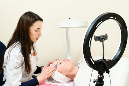 A beautician performs a face massage by rubbing cream into the skin, in the foreground is an LED lamp, a portrait of a beautician.の写真素材