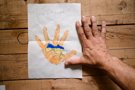Kyiv, Ukraine July 1, 2022: Children's drawings on the theme of war, Ukrainian defender holds drawings from children in his handsのeditorial素材