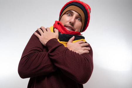 A man on a white background in several hats and scarves warms his hands, warm outerwear for winter, photo for advertising.の写真素材