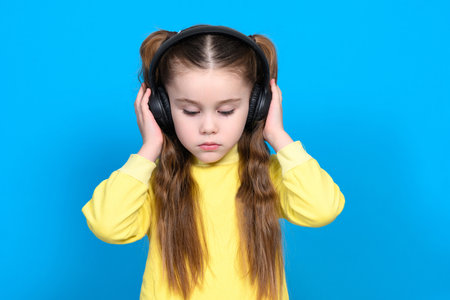A girl on a blue background in a yellow sweater with headphones on her head, wireless headphones in...