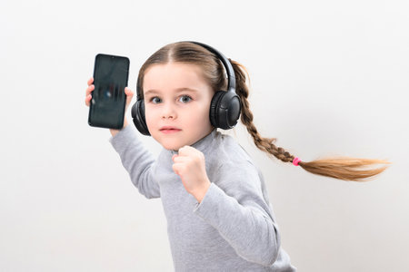 Happy little girl with wireless headphones and phone, portrait of girl with pigtails on white...