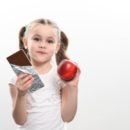Portrait of a little girl on a white background, she chooses chocolate over an apple, healthy food vs junk food.の写真素材
