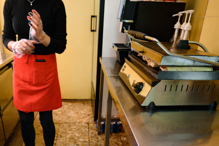 A girl is waiting for shawarma, which is being prepared on the grill, the kitchen of a fast food...