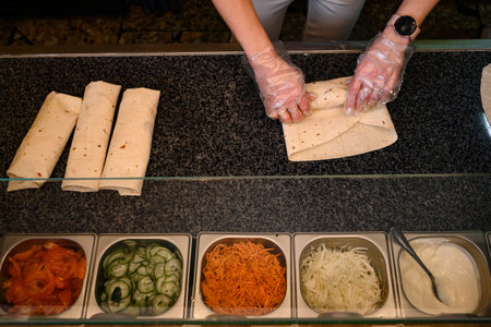 A cook in disposable gloves spins shawarma on a work surface, an establishment of fast food...