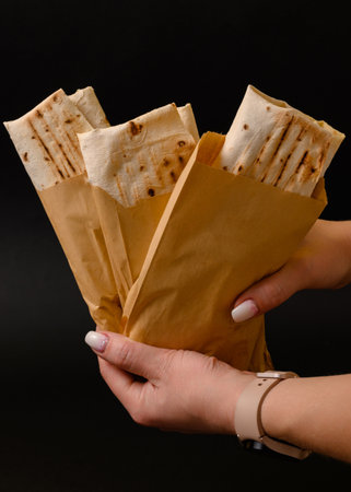 The girl holds three shawarmas in paper bags in her hands on a black background, copy space and black background.の写真素材