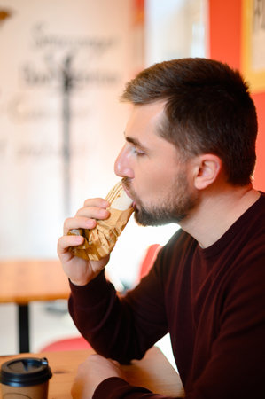 A man sits in a fast food restaurant and bites shawarma against a red wall background, shawarma for a quick snack.の写真素材