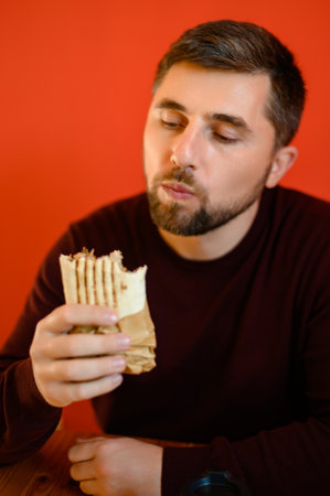 A man with a beard is sitting on a chair and eating shawarma, a quick, tasty and healthy snack in a fast food restaurant.の写真素材