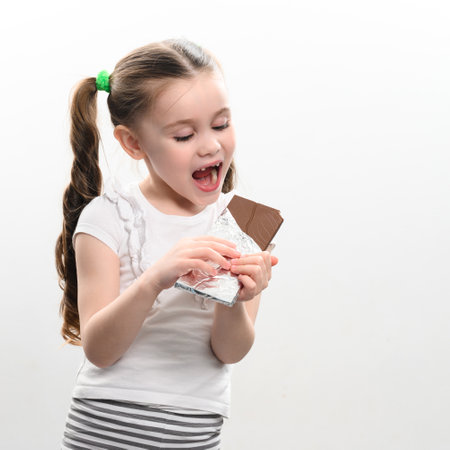 A happy and smiling little girl has a chocolate bar, portrait of a child with chocolate on a white background, baby teeth and chocolate.の写真素材