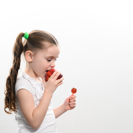 A child bites a big red apple and holds a lollipop in his hand on a white background, healthy teeth and healthy eating.の写真素材