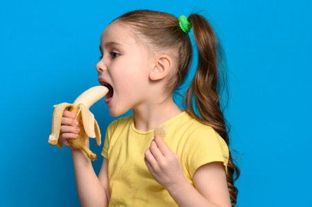 On a blue background, a girl holds one banana and potato chips in her hands, an idea for healthy and unhealthy food for children.の写真素材