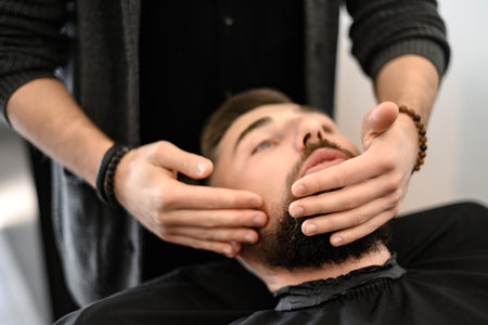 A barber massages and rubs a male clients beard after applying moisturizing oilの写真素材