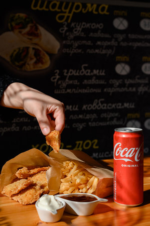 Ivano-Frankivsk, Ukraine March 26, 2023: Female hand dips chicken nuggets in sauceのeditorial素材