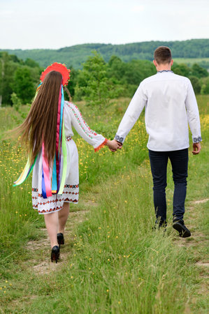 A boy and a girl walk hand in hand through the field, they are dressed in Ukrainian national clothes, a boy and a girl walk.の写真素材