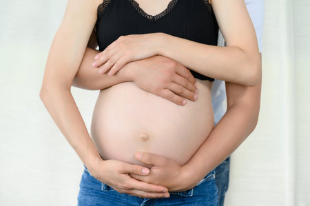 Bare belly of a pregnant woman, a married couple is waiting for the birth of their child, hands on the belly of a pregnant woman.の写真素材