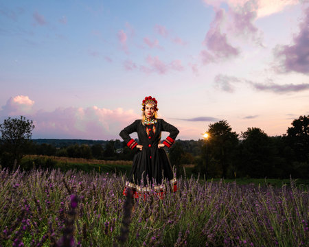 A girl in a chelsea headdress and a black dress decorated with red embroidery stands between lavender bushes.の写真素材