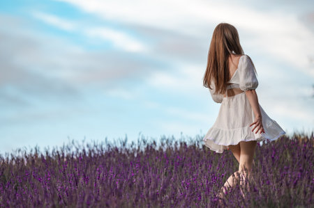 A beautiful girl walks in a white dress in a lavender field, aromatherapy in a lavender field.の写真素材