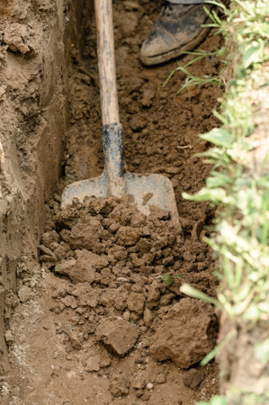 A man shovels a trench for drainage and sewage, close up.