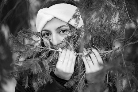 Winter portrait of a girl looking through spruce branches, close up portrait.