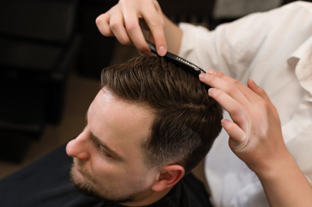 Hair styling with a comb, combing the client's hair by a stylist. Haircut of a visitor in a barbershop.の写真素材