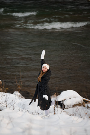 Beautiful girl in winter clothes in the forest near the river in winter, winter white headband and white gloves.の写真素材