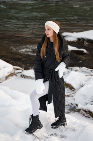Beautiful girl in winter clothes in the forest near the river in winter, winter white headband and white gloves.の写真素材