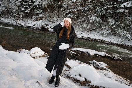 Winter photo shoot for a young girl near a river in the forest, a girl in white tights, gloves and a white headband with a black jacket.の写真素材