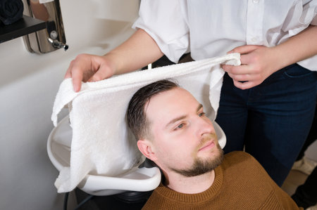 A hairdresser wipes a client man head with a white towel after washing in a barbershop.の写真素材