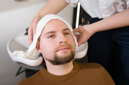 A hairdresser wipes a client man head with a white towel after washing in a barbershop.の写真素材