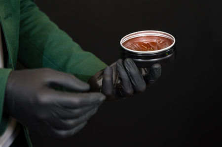 A barber in black gloves takes some pomade wax from a tin can to style a client's hair.の写真素材