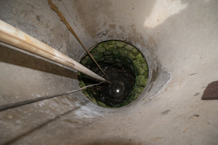 A view of a village well with water, there is a cord and a hose in the well.の写真素材