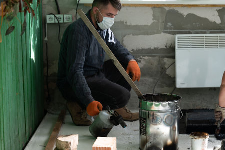 A man uses a kerosene lamp to heat resin in a bucket, working with waterproofing and resin, a master in his own right.の写真素材