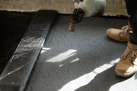 Waterproofing a floor in a house, a man heats a roll of bitumen with a kerosene lamp to glue it to the resin.の写真素材