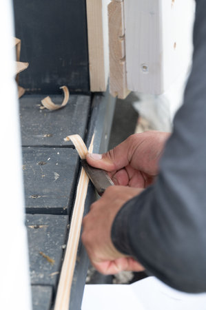 A man uses a carpentry tool, a milling cutter, to cut out a threshold under the door, moments in the...