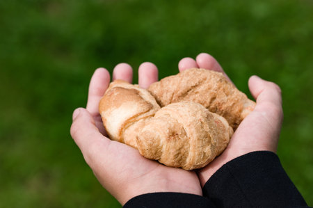 Two hands gently cradle a trio of golden-brown pastries against a vibrant green backdrop. The...