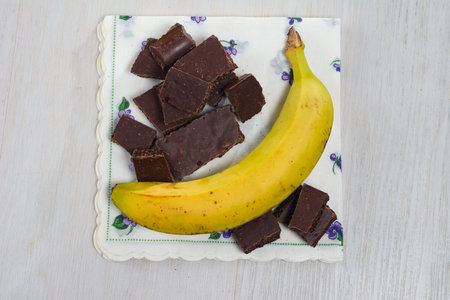 A ripe banana and chunks of dark chocolate rest on a decorative napkin, suggesting a sweet treat or snack combination.の写真素材