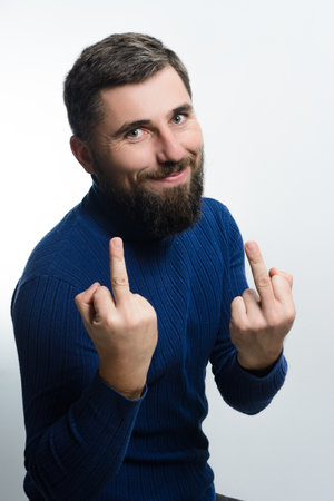 A bearded man in a blue sweater makes a gesture with both hands against a white background. He has a mischievous smile.の写真素材